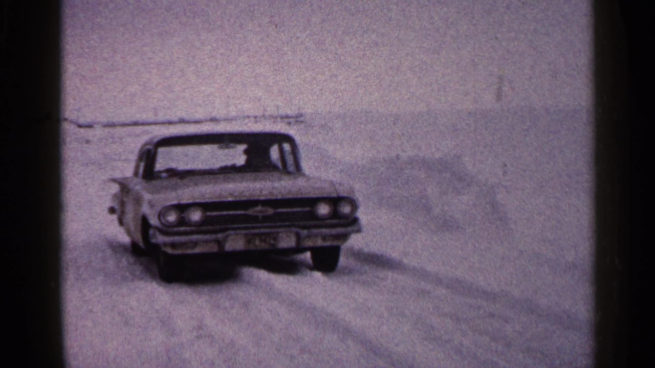 The sedan continues across the frozen lake in Duluth, with the driver faintly visible through the windshield.