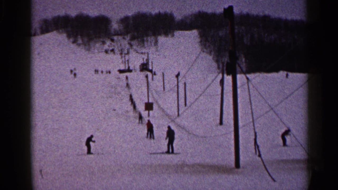 Skiers wait on a snowy slope near lift poles and cables.