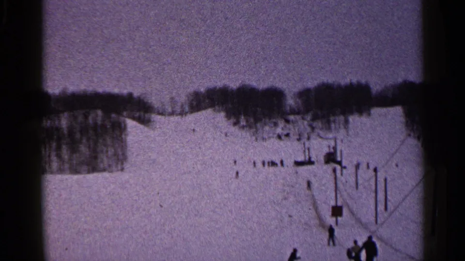 Home-movie view of a Duluth ski slope in 1960, with distant people, lift equipment, and trees along the horizon.