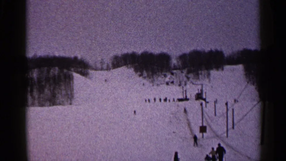 1960 Duluth ski-area frame showing people near the lower edge of the slope and lift poles rising through the snow.