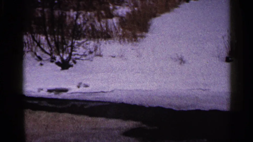 1960 Duluth winter frame showing a snowy bank, bare shrubs, and a dark water channel along the bottom of the 8mm frame.