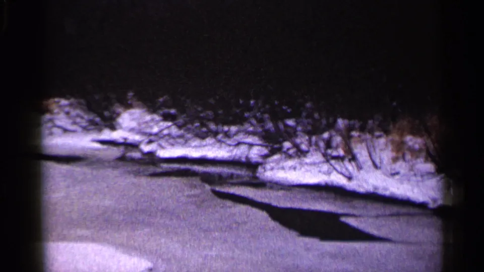 1960 Duluth winter frame with frozen water, snow-covered bank, bare brush, and deep shadow under dark exposure.