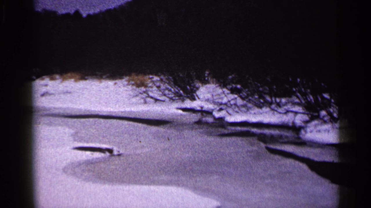 Frozen river bordered by snow and bare trees under a dark upper frame.
