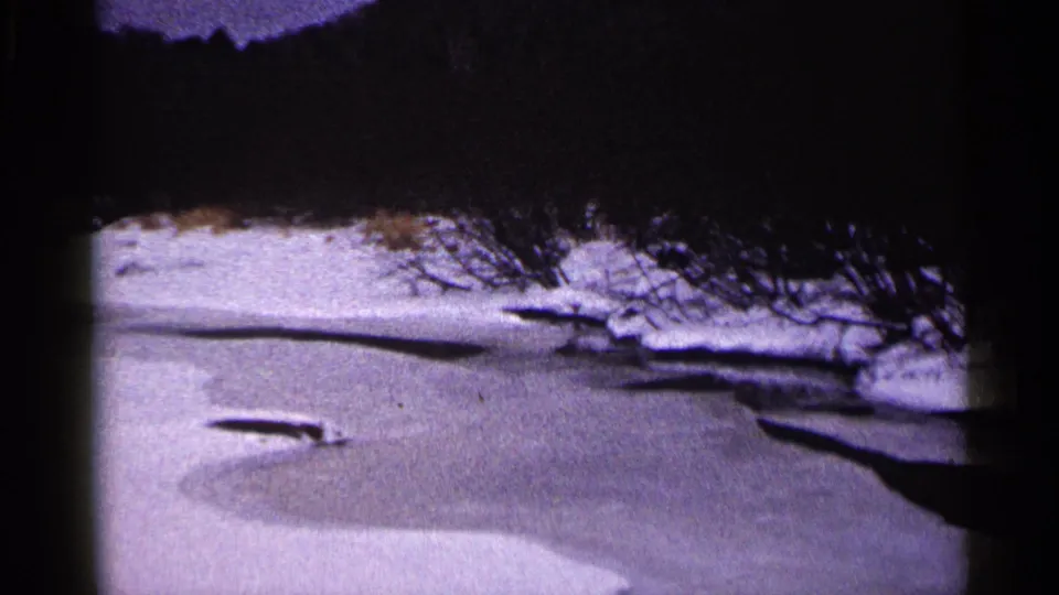 Duluth winter river view on grainy 8mm footage, with snow-covered banks and bare trees along the water.