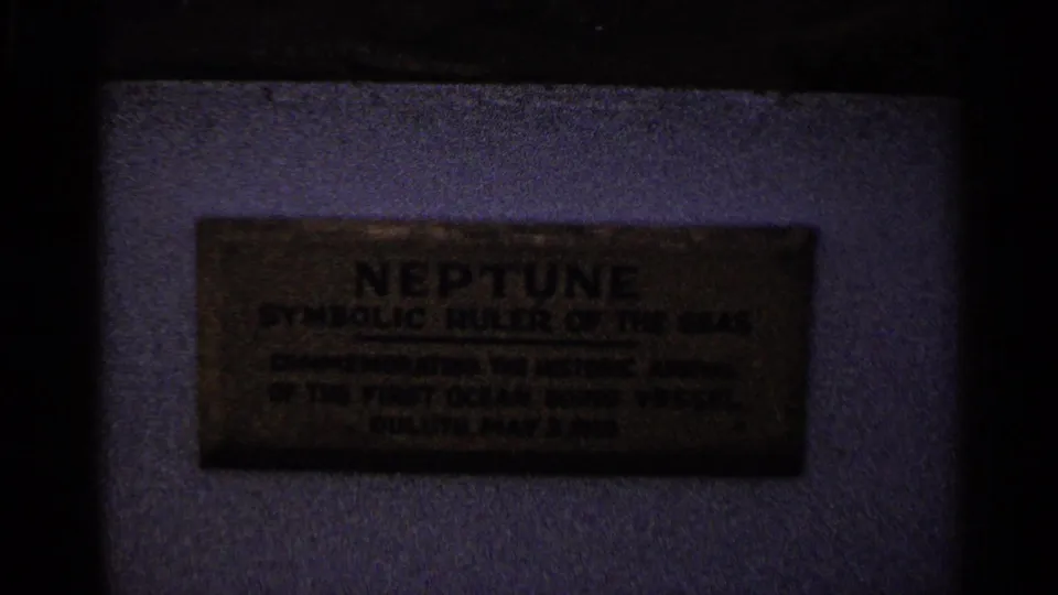 Close-up of a Neptune commemorative plaque on a wall, partially dark and soft in 8mm footage.