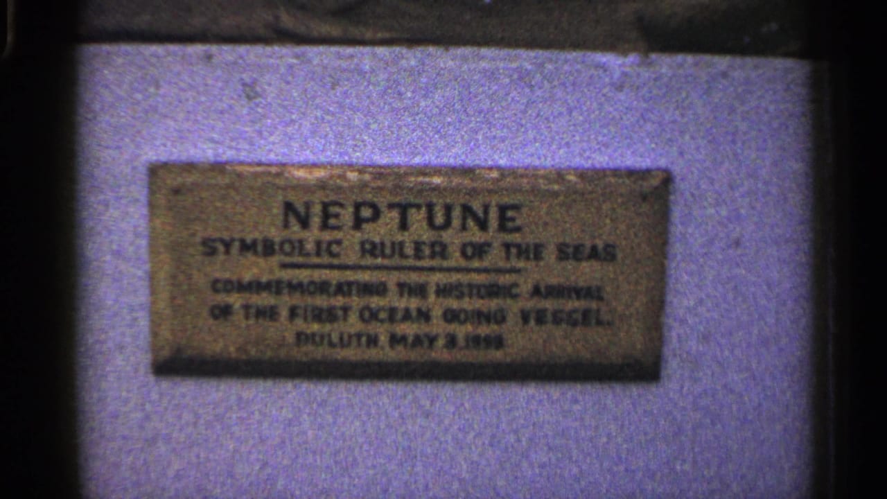 Duluth home-movie frame with the Neptune plaque centered against a pale mounting surface.