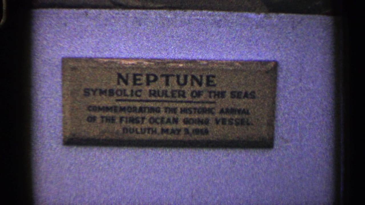 1960 Duluth 8mm close-up of the weathered Neptune commemorative plaque before the wider statue view.