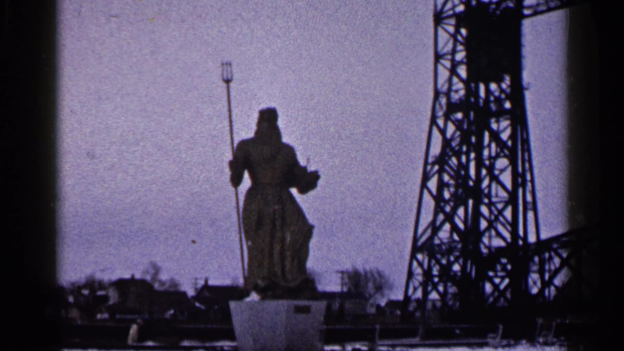 1960 Duluth frame with the trident-holding statue silhouetted near an industrial bridge tower under a muted sky.