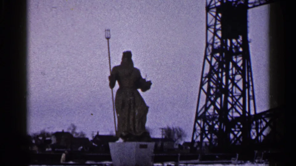1960 Duluth frame with the trident-holding statue silhouetted near an industrial bridge tower under a muted sky.