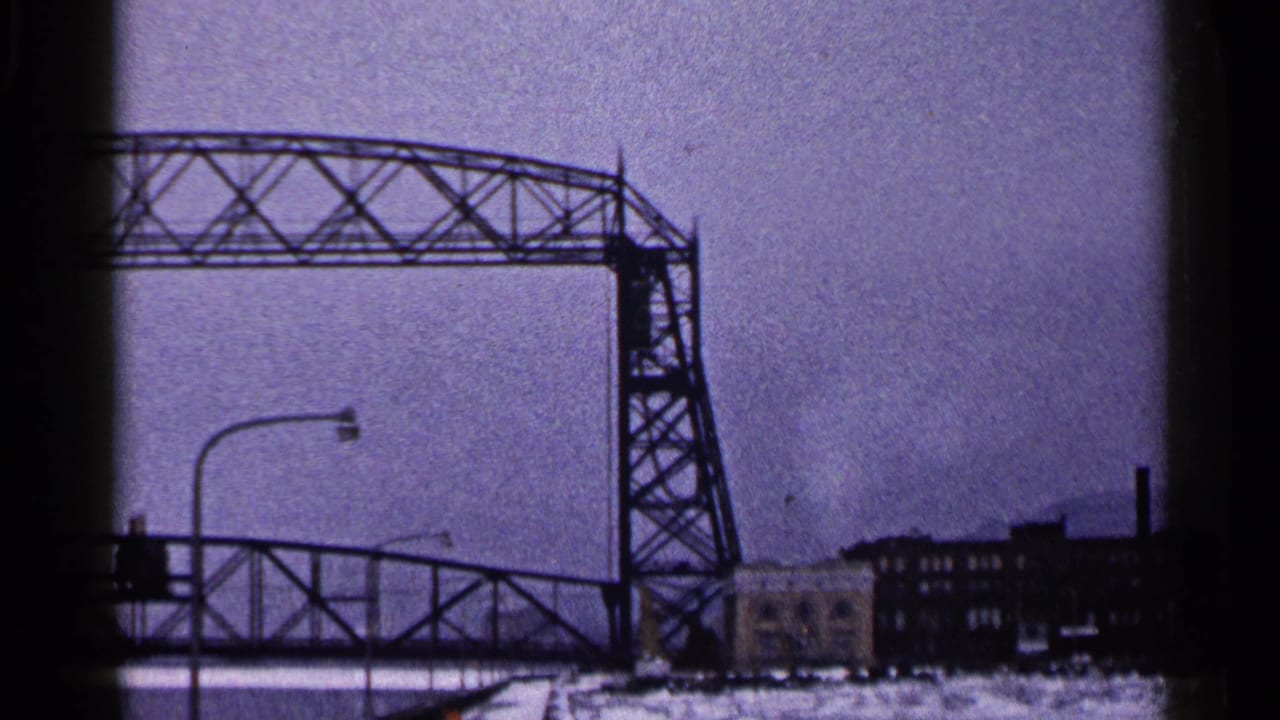 Duluth Aerial Lift Bridge raised in winter, with the lower roadway stopped and industrial waterfront buildings visible below.