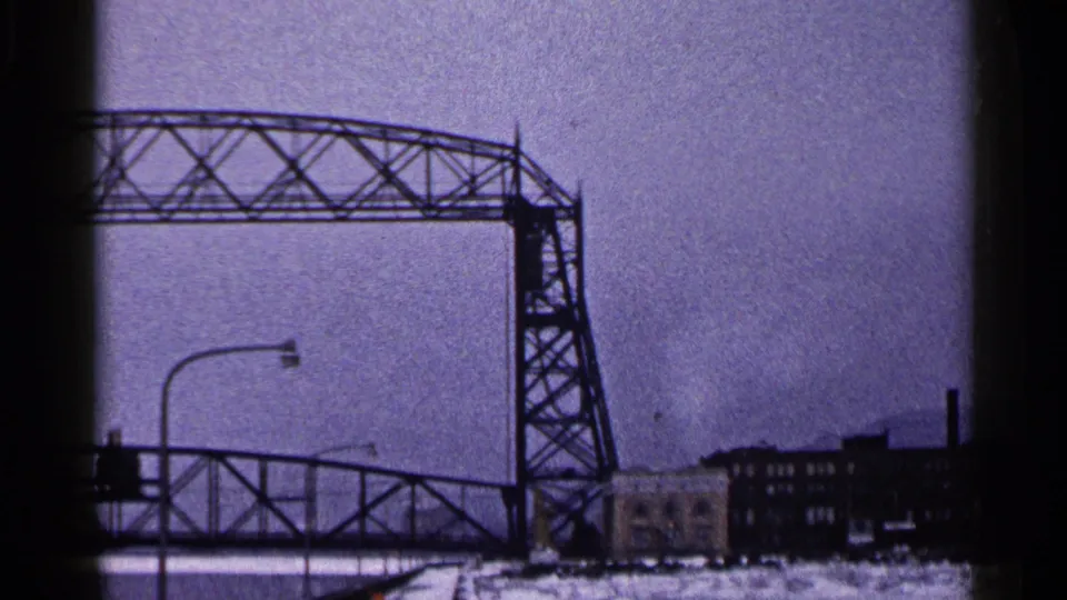 Duluth Aerial Lift Bridge raised in winter, with the lower roadway stopped and industrial waterfront buildings visible below.