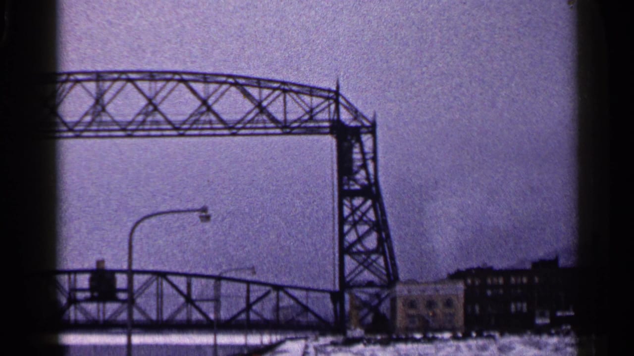 The Duluth lift bridge stays open above the roadway, with snow, street lighting, and industrial buildings under a gray sky.
