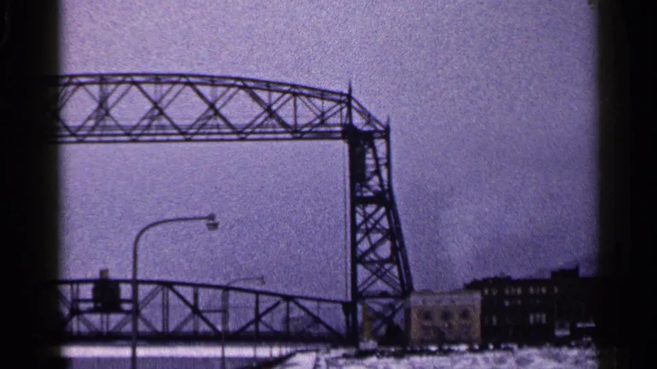 The Duluth lift bridge stays open above the roadway, with snow, street lighting, and industrial buildings under a gray sky.