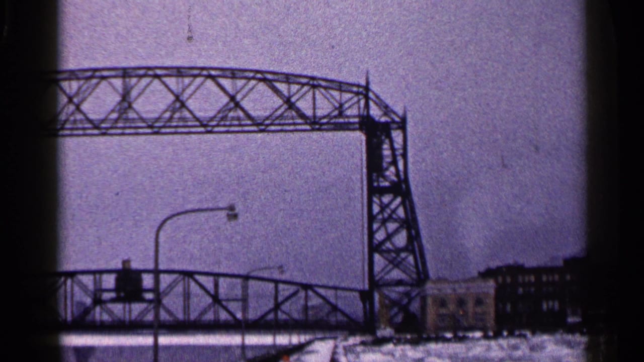 A closer home-movie view of the raised Duluth lift bridge shows the roadway railings, streetlights, snow, and harbor-side buildings.
