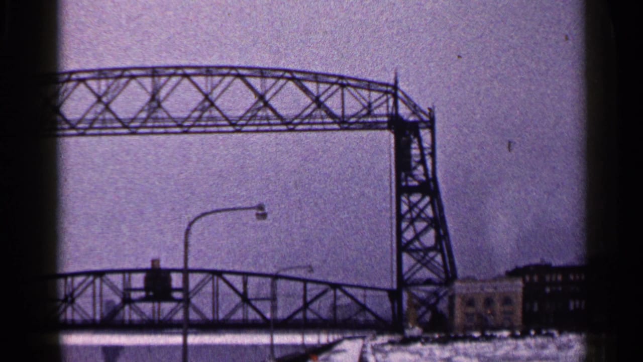 The Duluth Aerial Lift Bridge remains raised at the end of the clip, framed by a snowy roadway, streetlights, and waterfront buildings.
