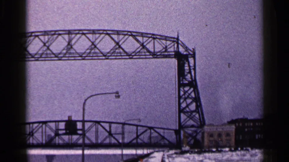 The Duluth Aerial Lift Bridge remains raised at the end of the clip, framed by a snowy roadway, streetlights, and waterfront buildings.