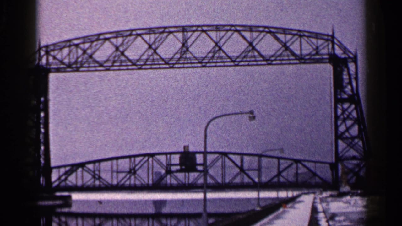 Steel truss bridge seen over snow and streetlights under an overcast sky.