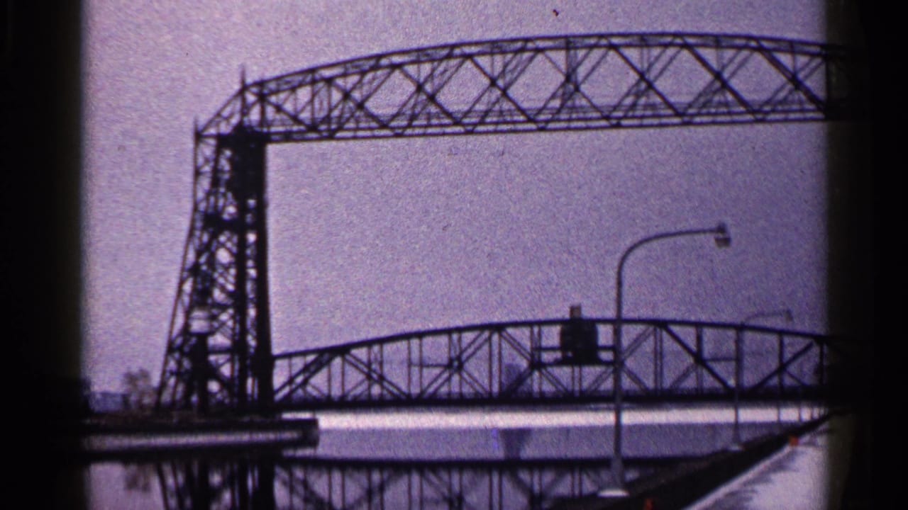 1960 Duluth frame showing the bridge tower, lattice span, snow-covered edge, and foreground streetlights.