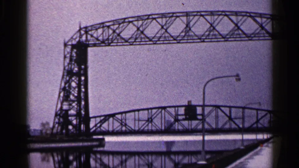 1960 Duluth frame showing the bridge tower, lattice span, snow-covered edge, and foreground streetlights.
