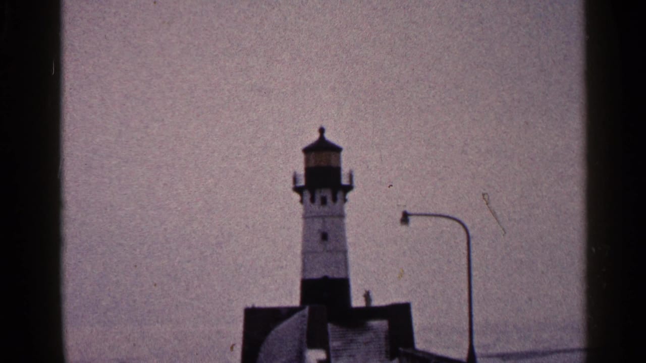 Duluth harbor lighthouse view from 1960 home-movie footage, with a pier structure, streetlight, and muted winter sky.