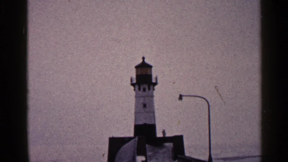 Duluth harbor lighthouse view from 1960 home-movie footage, with a pier structure, streetlight, and muted winter sky.