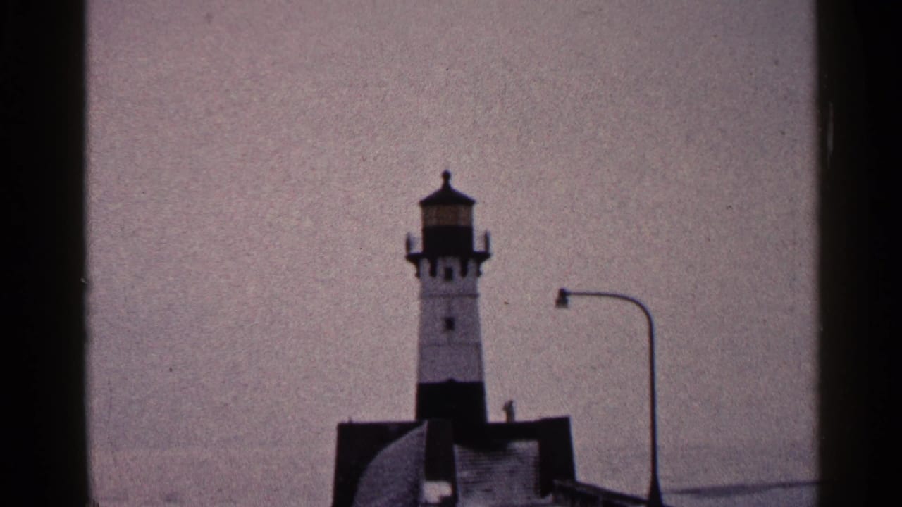 Lighthouse on a pier beneath an overcast sky with a curved lamppost nearby.