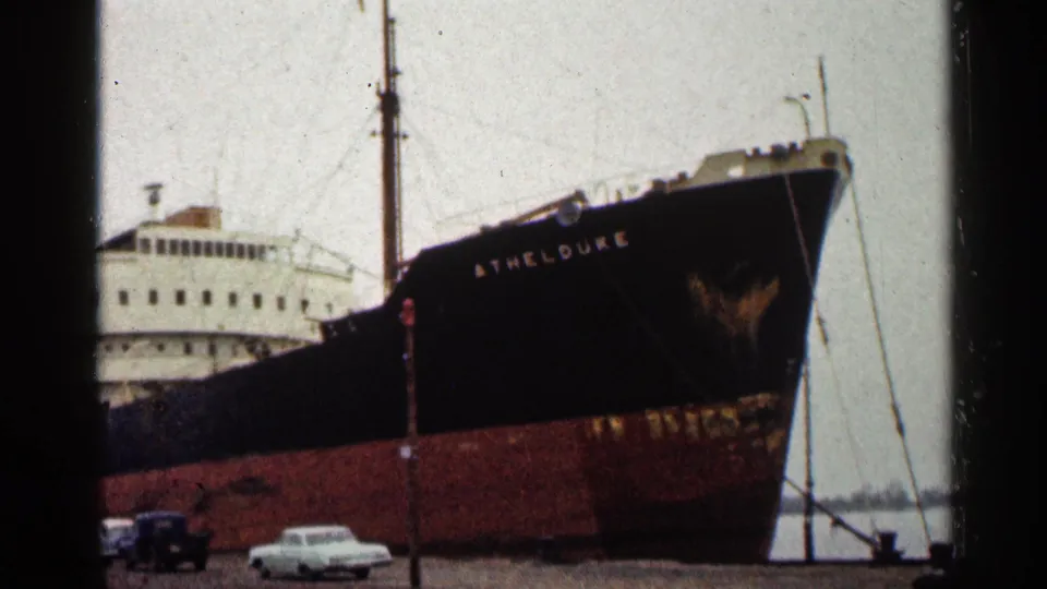 1960 Duluth harbor view of the ATHELDUKE docked beside cars, with the ship bridge and bow visible.