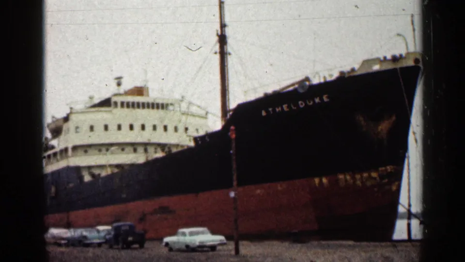 1960 Duluth dock view of the Athel Duke freighter, with its dark hull, white superstructure, mast, and parked cars visible.