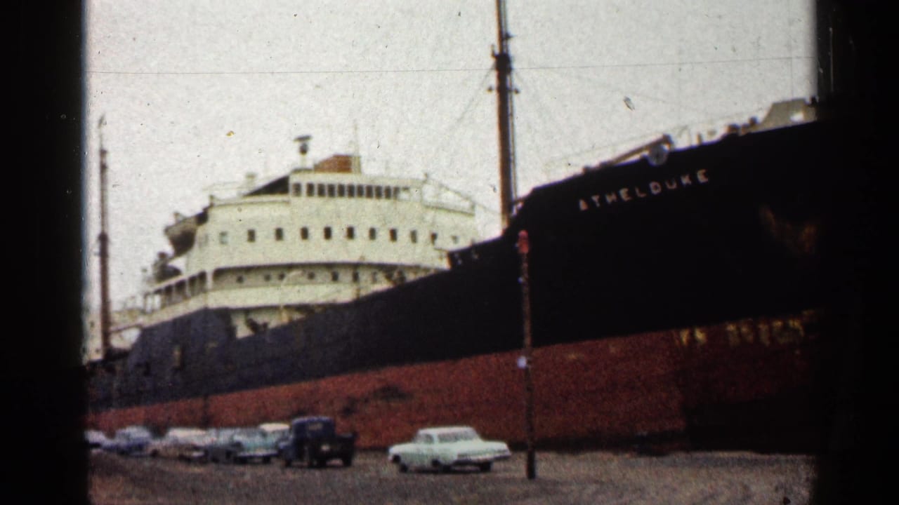 Freighter hull and superstructure beside a line of parked cars.