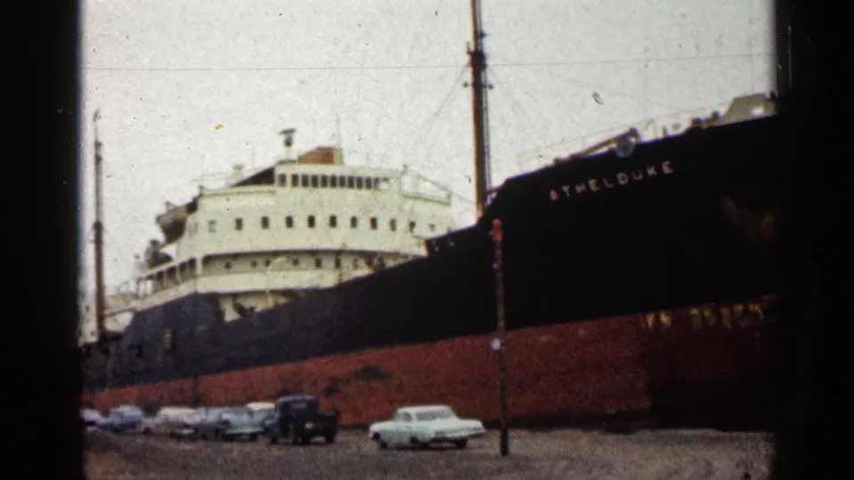 The Athel Duke remains docked in Duluth, with its name on the dark bow and several early-1960s cars along the waterfront.