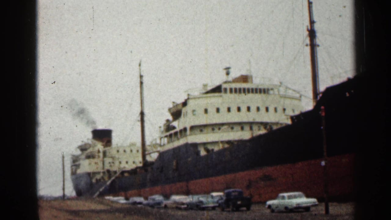 1960 Duluth waterfront view of a large docked passenger ship with smoke from its stack and period cars along the shore.