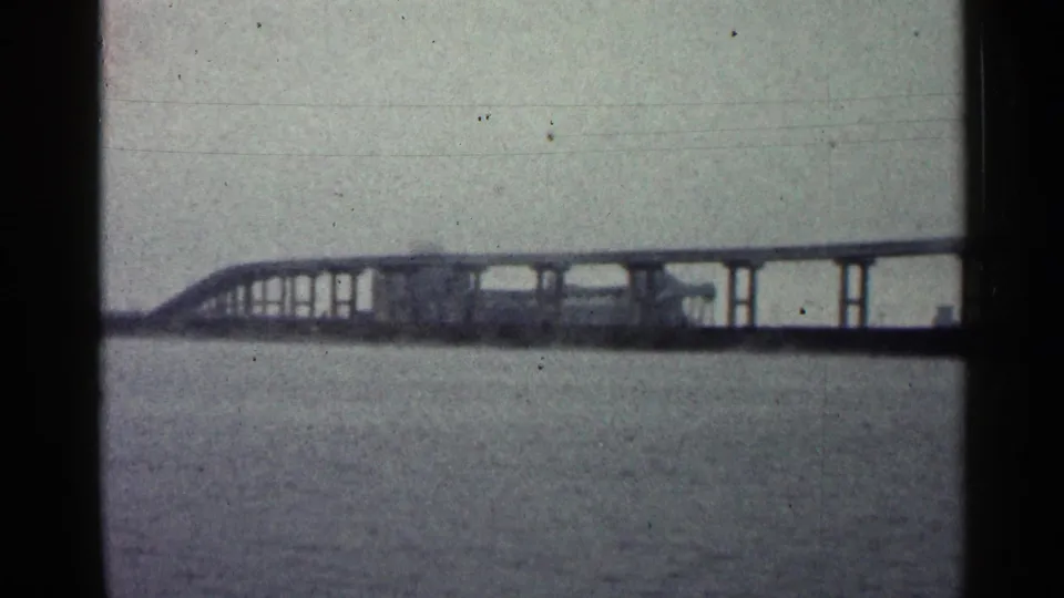 Distant 1960 Duluth view of a long bridge on pilings spanning open water under overcast light.