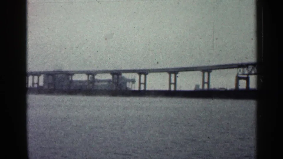 1960 Duluth home-movie frame showing the bridge's long low span and pilings over water.