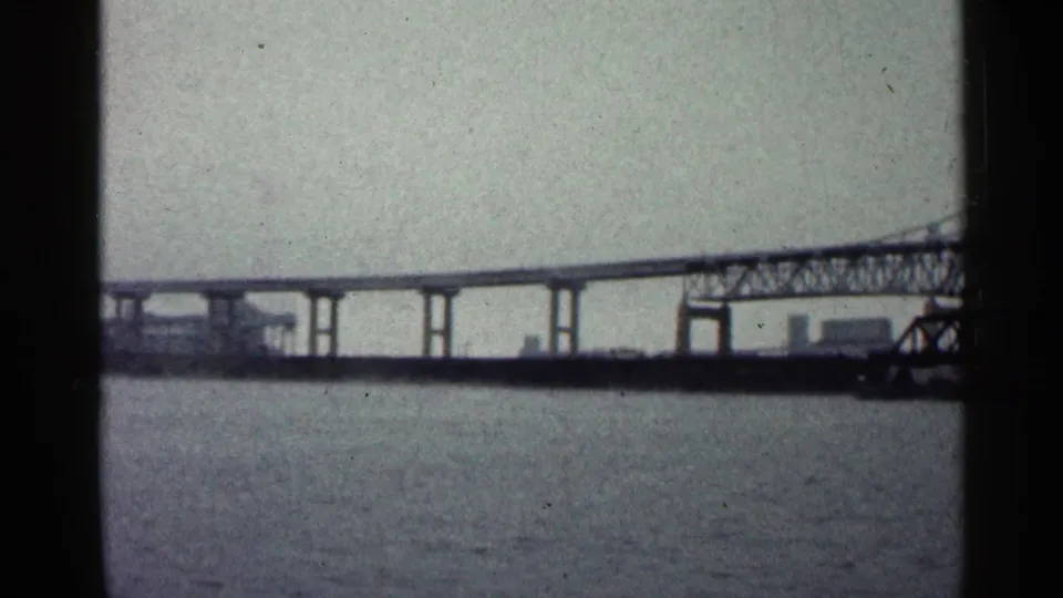 1960 Duluth home-movie frame showing a steel truss bridge and roadway span across open water.
