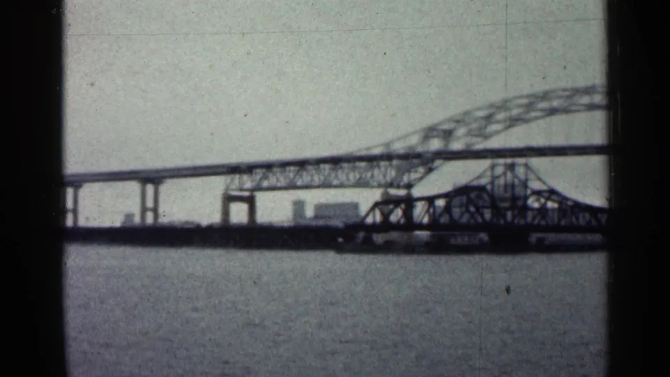 A 1960 Duluth frame shows bridge framework over water, including a lower truss structure near the main span.