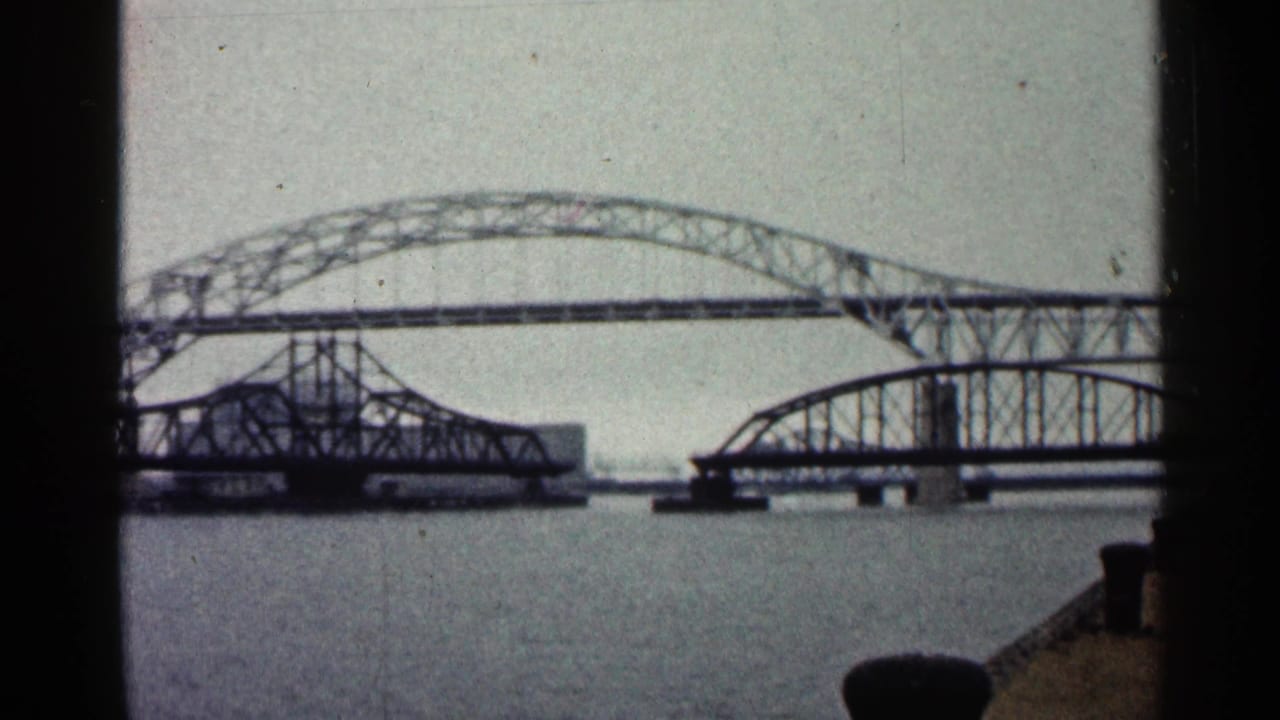 Duluth riverfront frame showing overlapping steel bridge spans, open water, and the edge of a concrete waterfront pier.