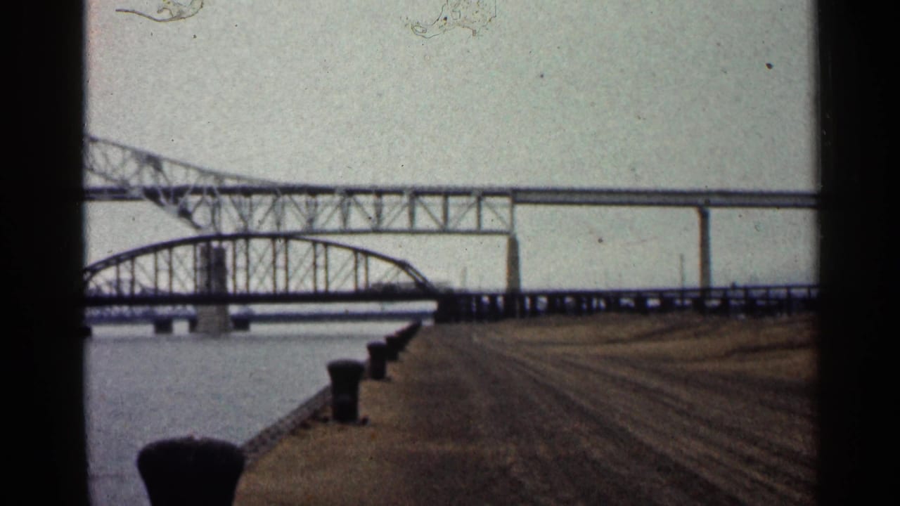 Duluth waterfront frame with a steel truss bridge over the river and a concrete pier with bollards in the foreground.