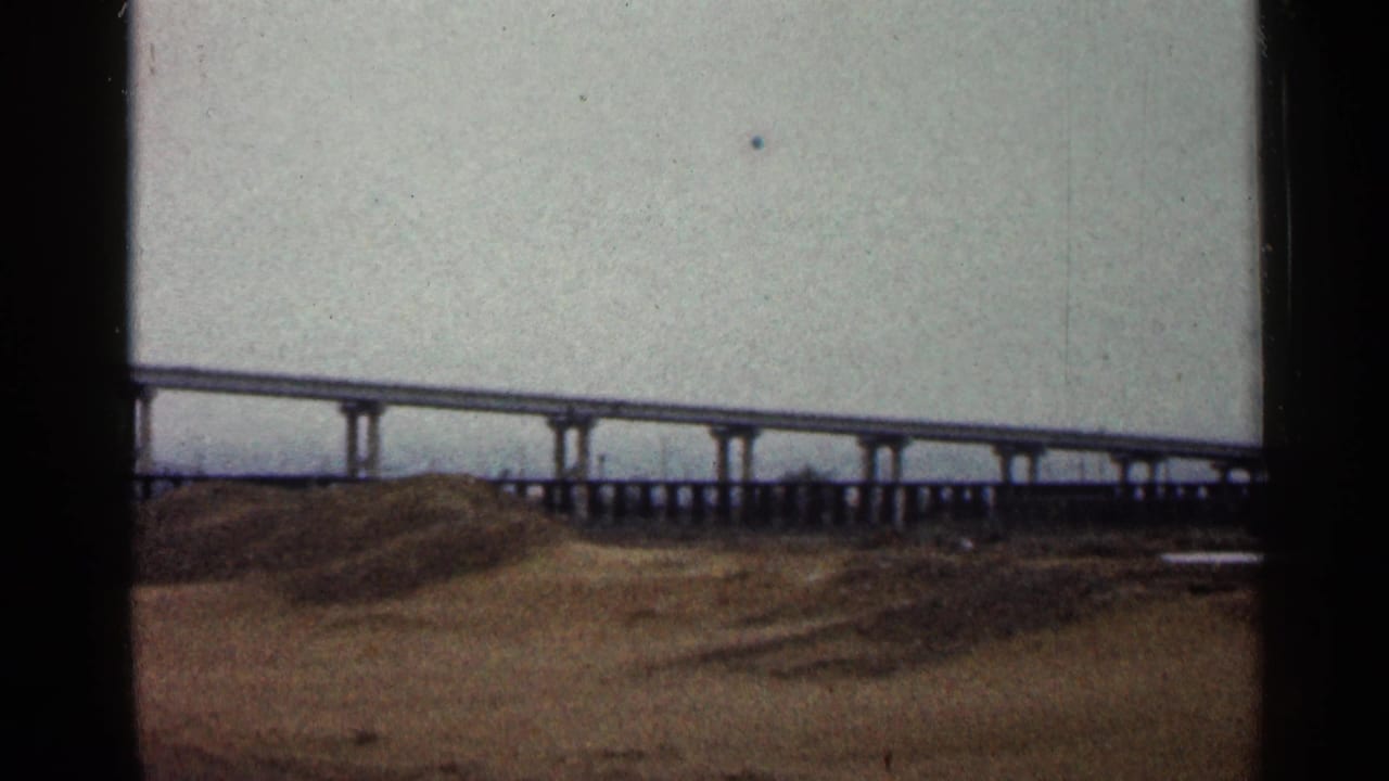 1960 Duluth frame with the elevated roadway continuing across the horizon above an open brown field.