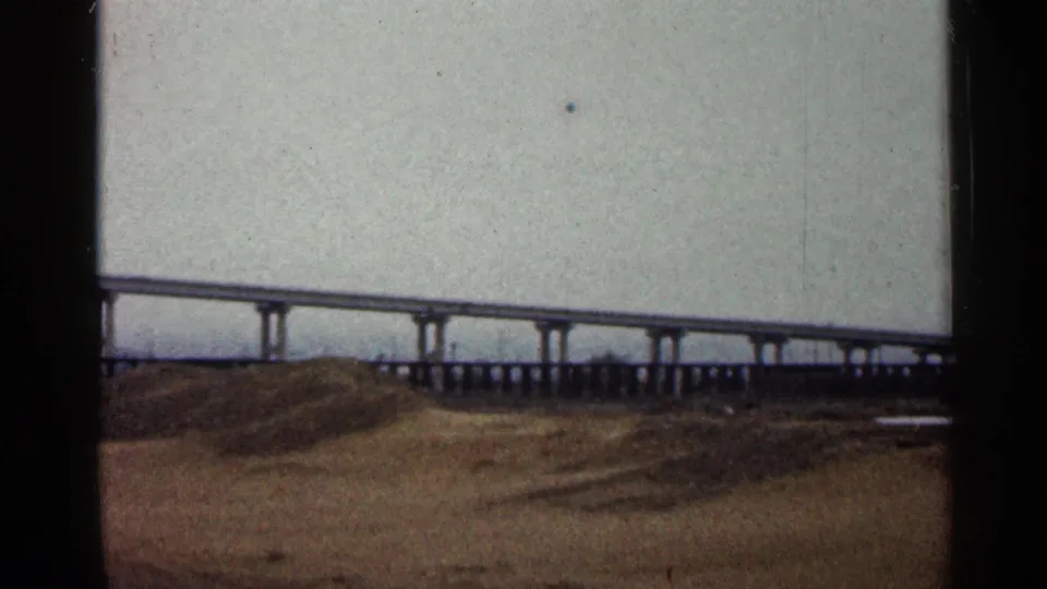 1960 Duluth frame with the elevated roadway continuing across the horizon above an open brown field.