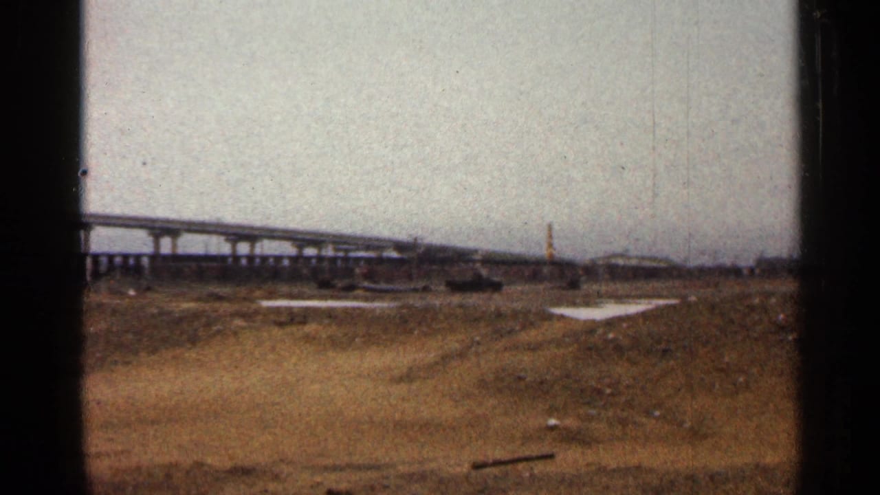 Distant bridge and open dirt area under an overcast sky.