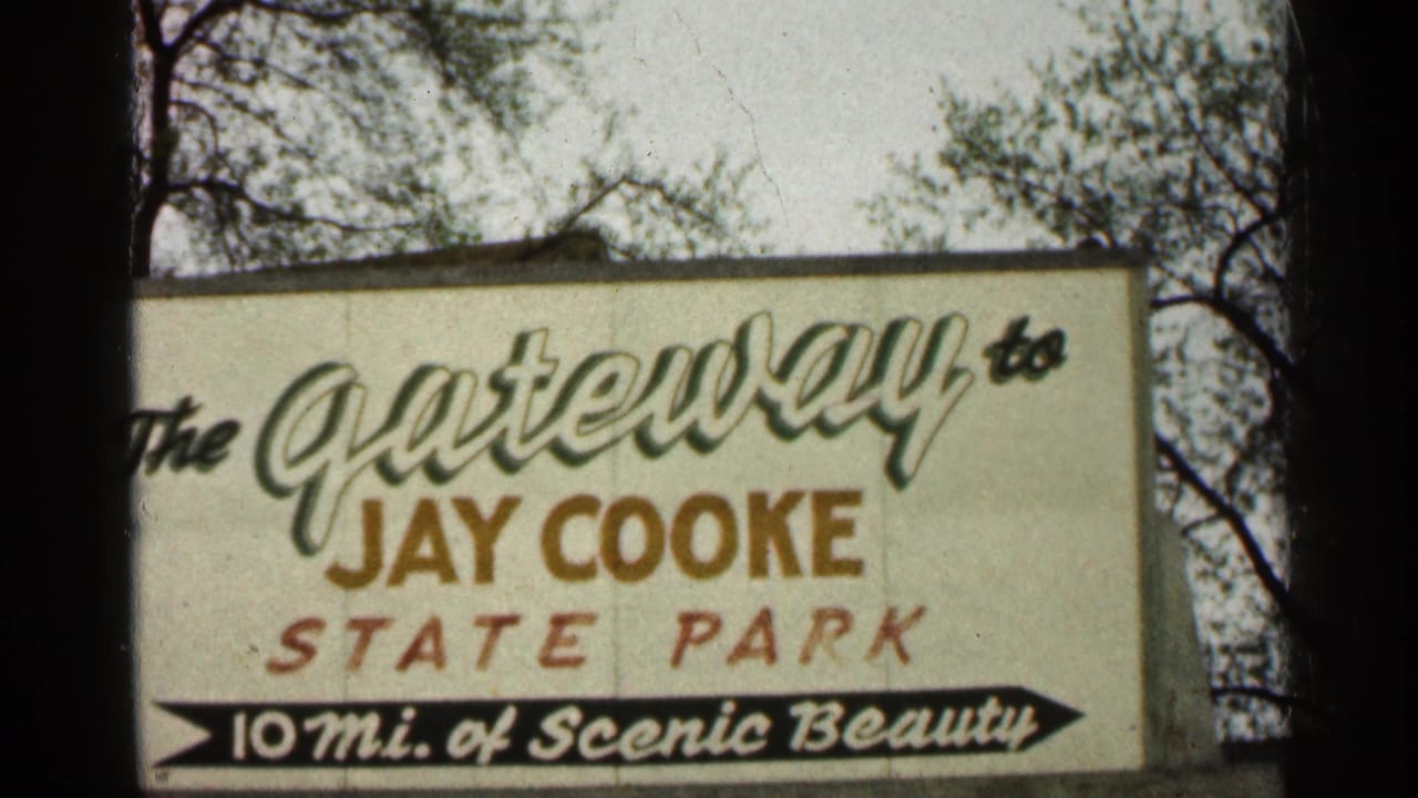 1960 Duluth-area frame of a roadside sign for Jay Cooke State Park, with decorative lettering and bare branches behind it.