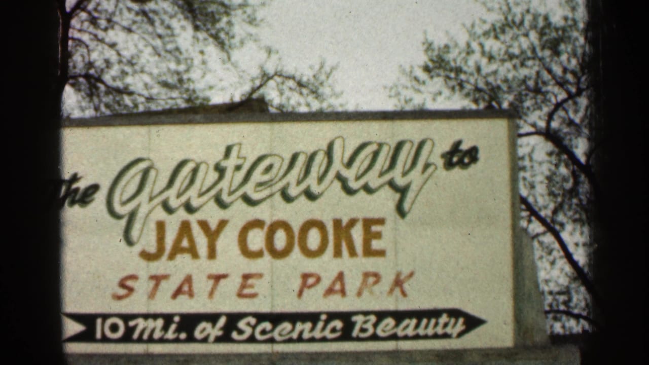 1960 Duluth-area frame with the Jay Cooke State Park sign filling the view, bordered by tree branches and dark film edges.