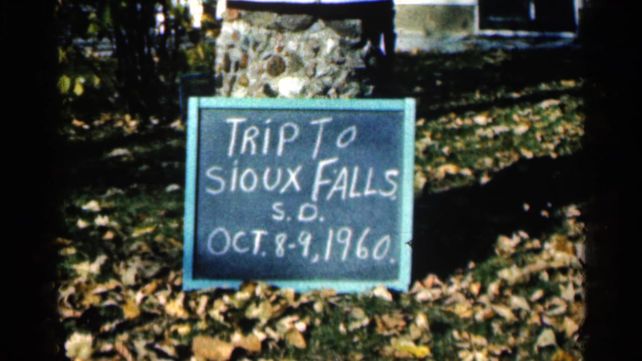 Handwritten sign reading Trip to Sioux Falls, S.D., Oct. 8-9, 1960, placed outdoors on fallen leaves.