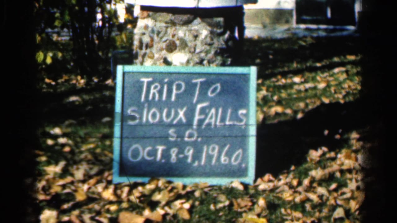 Handwritten Sioux Falls trip sign resting outdoors among fallen leaves.