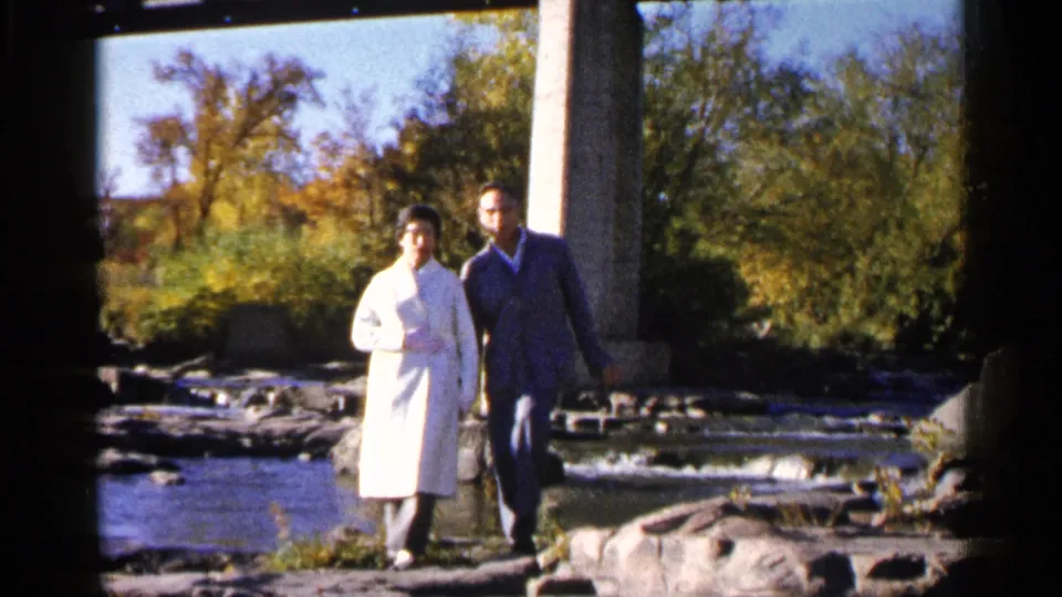 In Sioux Falls, South Dakota, a couple walks beside a rocky stream beneath bridge supports in 1960s 8mm home-movie footage.