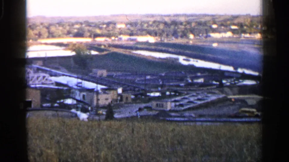 Sioux Falls 1960 8mm frame showing an elevated look over industrial buildings, open ground, water, and distant residential areas.