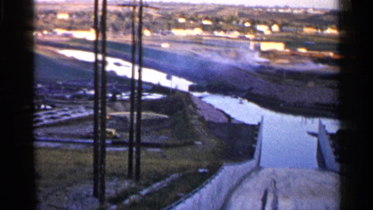High-angle view of a winding water channel with concrete banks and utility poles.