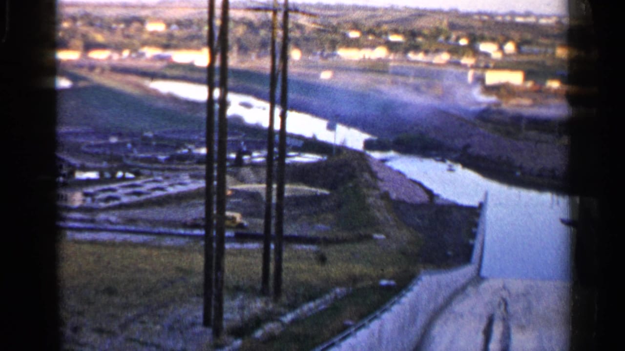 Similar high-angle view across the channel, embankments, poles, and distant buildings.