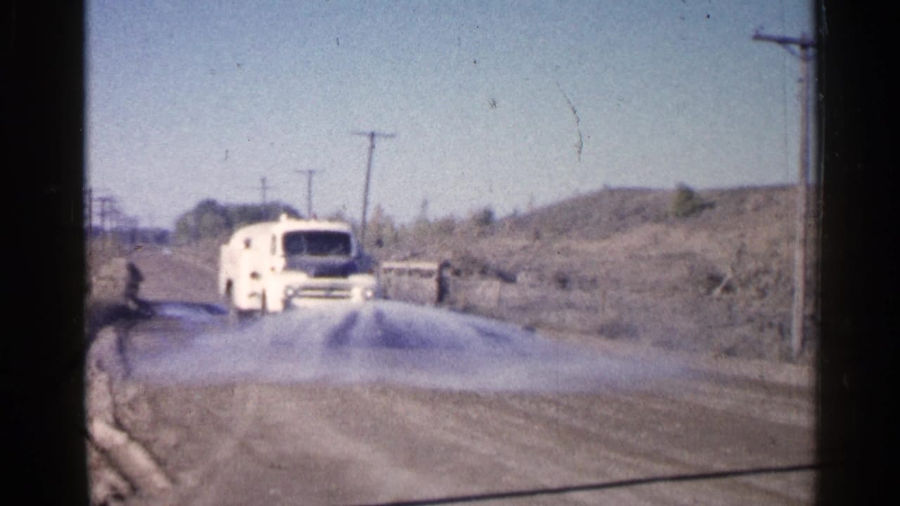 White utility van spraying water along a dusty rural road.