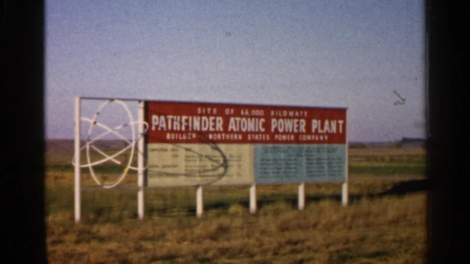 A steady 1960 home-movie view holds on the Pathfinder Atomic Power Plant site sign with atomic graphic and surrounding field.